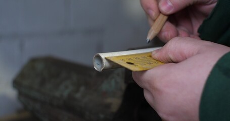 Men's hands measure a piece of pipe with a ruler and make a note with a pencil. A man in a workshop takes measurements of a water pipe for a house.