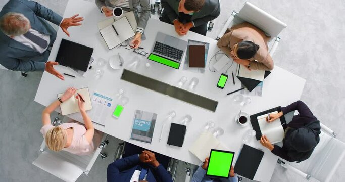 Laptop, tablet and green screen, business meeting from above with mockup and chromakey. Financial reports, notes and a businessman leading audit. Diversity, auditors and men and women at office table