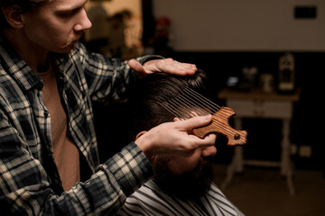 barber accurate doing hair styling to man with comb with long metal teeth