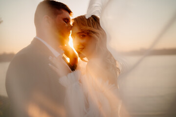 the bride and groom under the veil on the sunset by the river