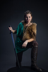 A young brave Viking heroine with a sword in hands on a dark background. A young woman in a suit in Scandinavian or fantasy style