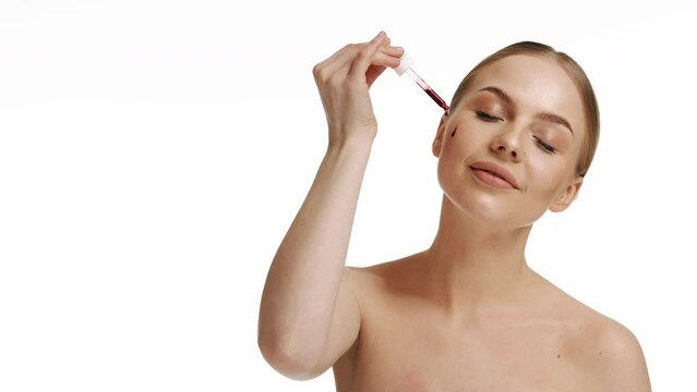 Beauty woman with freckles, naked shoulders and nude face, apply serum vitamin c, argan oil tea tree ingredients in pippette dropper under eye, treating skin for nourishing and moisturizing effect.