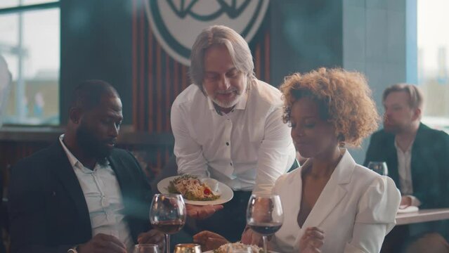 Waiter serving food for African-American couple in restaurant. Realtime