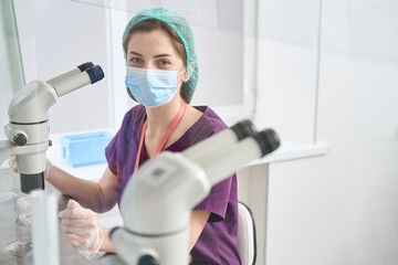 Laboratory employee sits at a powerful microscope