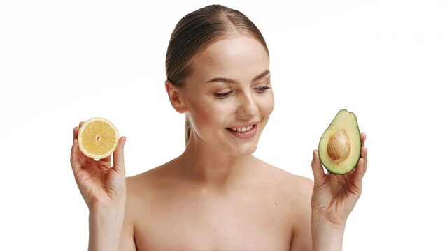 A beautiful young blonde girl holds half an avocado and half a lemon in her hands. Isolated on white background. The concept of health, body care, nutrition