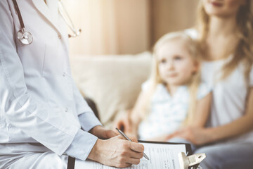 Doctor and patient. Pediatrician using clipboard while examining little girl with her mother at home. Happy cute caucasian child at medical exam. Medicine concept