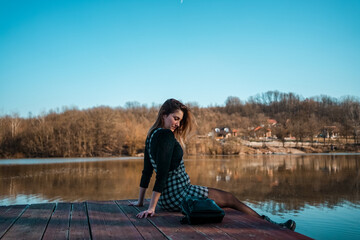Young woman sitting on lake pier, smiling and enjoying in beautiful landscape.