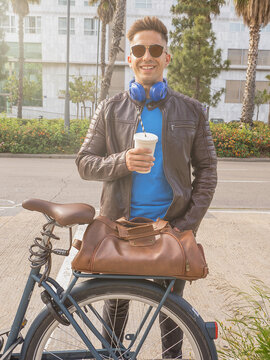 Retrato vertical de un chico joven sonriendo a c&aacute;mara con una vaso de batido en la mano y auriculares azules. D&iacute;a soleado.