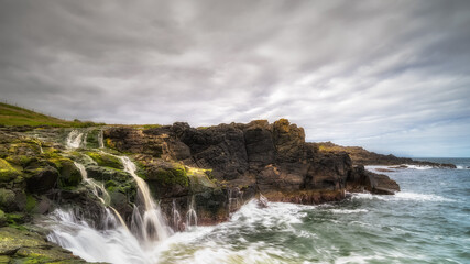 Fototapeta na wymiar Dunseverick Falls with small cliffs and streaks of water falling down to Atlantic Ocean, Causeway Coast, County Antrim, Northern Ireland