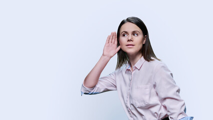 Young curious woman listening holding hand near ear, white background