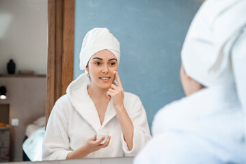 Young lady applying moisture on face in home bathroom