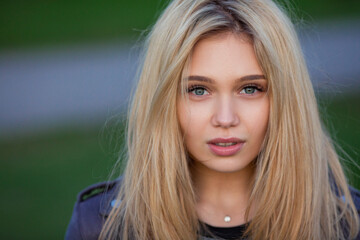Close-up portrait of a beautiful young slim caucasian blonde girl in grey dress and leather jacket...