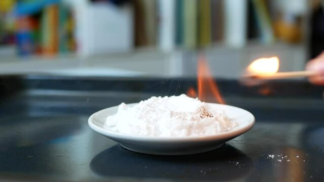 Hand ignites urotropin mixed with calcium gluconate and chemical decomposition reaction begins, selective focus. Concept of chemistry lesson, chemical experiment