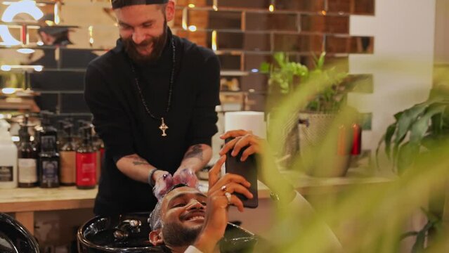 Medium shot of a hairdresser wahsing male client's hair while he is searching through his phone. High quality 4k footage
