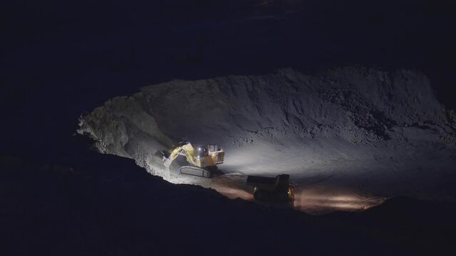 Work of trucks and the excavator in an open pit on gold mining at night, slow motion