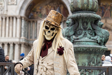 Fototapeta na wymiar Venice, Veneto, Italy - Feb 19, 2023: Masquerade man in a costume of skull wearing a top hat and a suit at San Marco Square during 2023 Venice Carnival celebrations