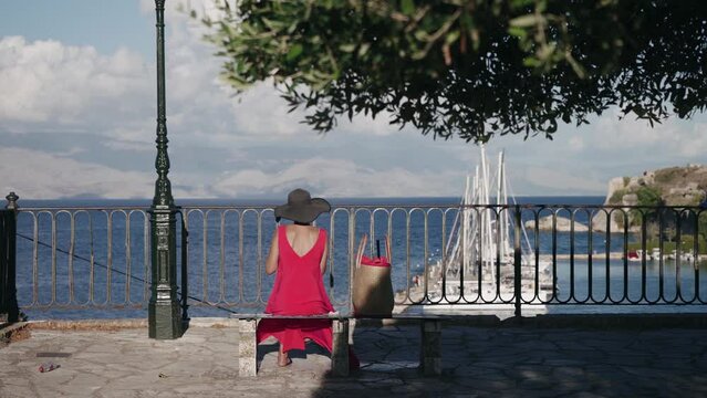 Tourist woman in dred dress enjoy view of the old Venetian fortress and yachts pier of Corfu Island town, Greece