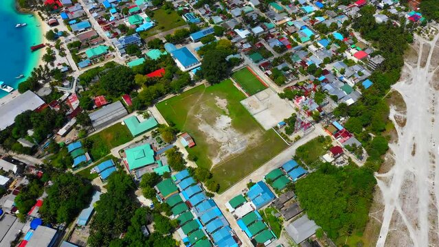 Aerial Shot Of Empty Sports Field Amidst Hotels On Island In Sea, Drone Flying Forward During Sunny Day - Thulusdhoo, Maldives