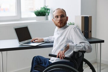 A man in a wheelchair looking at the camera businessman in the office working on a laptop online, social networks and startup, integration into society, work concept man with disabilities