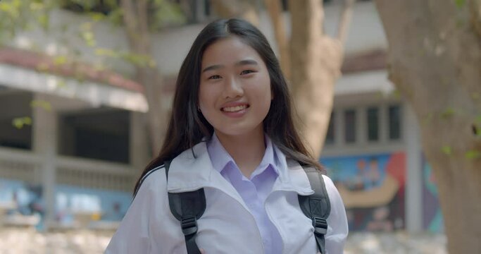 (Slow motion) A happy smiling cute Asian high school student girl who has long hair and a Chinese ethnicity face, standing in front of her school.
