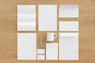 Blank corporate stationery set mockup with envelopes,  business cards, folder, trifold brochure, paper sheet, notebook, cup and pen on wooden background. Branding mock up. View directly above.