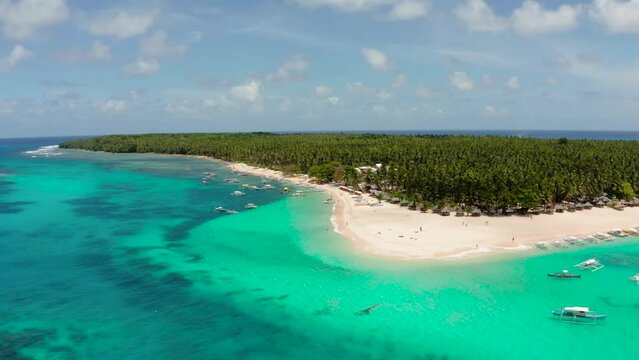 Beach with tourists and boats on a tropical island, clear blue water. Daco island, Philippines. Summer and travel vacation concept