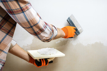 worker with putty knive near wall indoors, closeup. repair work of home.