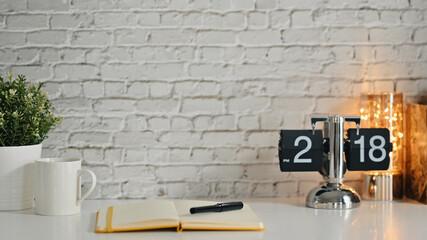 Home office desk with vintage flip clock and books and houseplant on white table against brick wall. Copy space for text