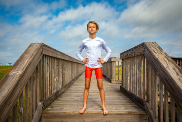 Young preteen boy swimmer with hands on hips looking out at the ocean