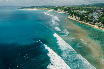 Ocean with perfect waves and coastline with hotels on Impossibles beach in Bali. Aerial view of tropical island
