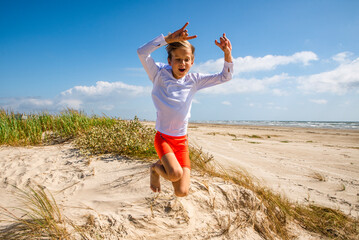 Fototapeta premium Young boy at the beach jumping from a sand dune 