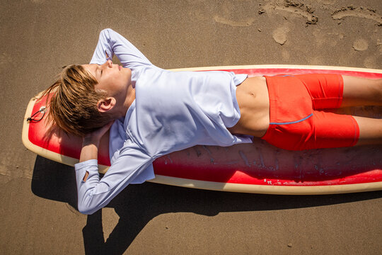 Young beach boy resting on his surfboard with his eyes closed