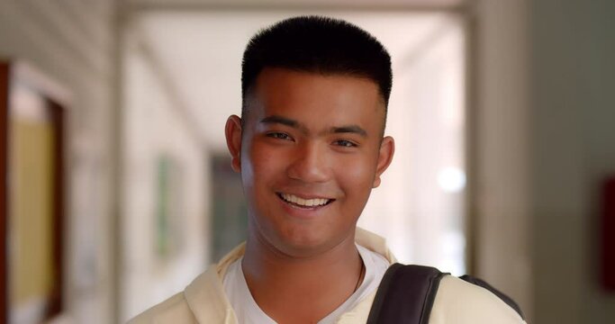 Slow motion scene of a happy smiling male high school student standing on a corridor in a school building with a laptop backpack.