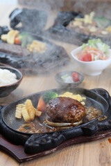 Japanese Hamburg steak with brown sauce and vegetables on a black hot plate in a Japanese restaurant