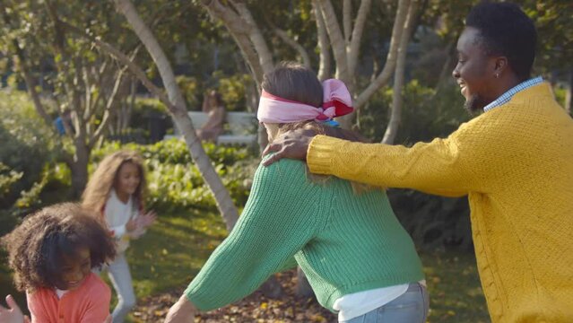 Happy mixed-race family playing blind man buff in park. Realtime