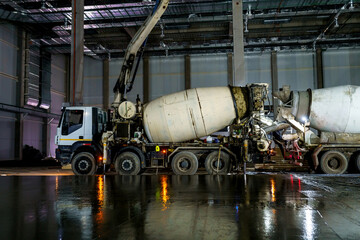 New concrete floor against the background of concrete mixers. Construction of an industrial building - obrazy, fototapety, plakaty