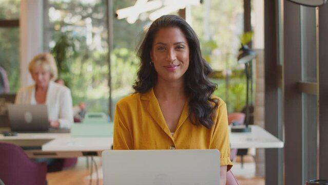 Portrait of mature businesswoman working on laptop at desk in modern office and smiling - shot in slow motion