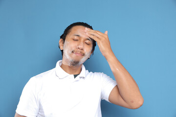 Close up portrait of young Asian man looking at camera, using facial clay mask, posing isolated over blue background. Beauty procedure and skincare routine concept. Horizontol shot