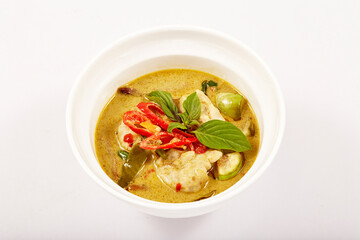 Green curry with fish balls and topped with red pepper and basil in a white bowl, coconut milk curry with green curry paste, fish ball made from Notopterus fish, very popular food in Thailand.