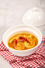 Sour soup with lotus stem and shrimps in a white bowl on table. local food of Thailand.