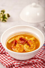 Sour soup with lotus stem and shrimps in a white bowl on table. local food of Thailand.