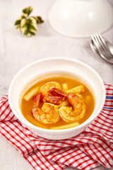 Sour soup with lotus stem and shrimps in a white bowl on table. local food of Thailand.