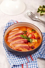 Red curry with roasted duck placed on a blue tablecloth, this food contains such as red curry paste, chili, tomato and pineapple.