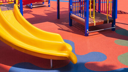 Slider with playground climbing equipment on colorful rubber floor in outdoors playground area - obrazy, fototapety, plakaty