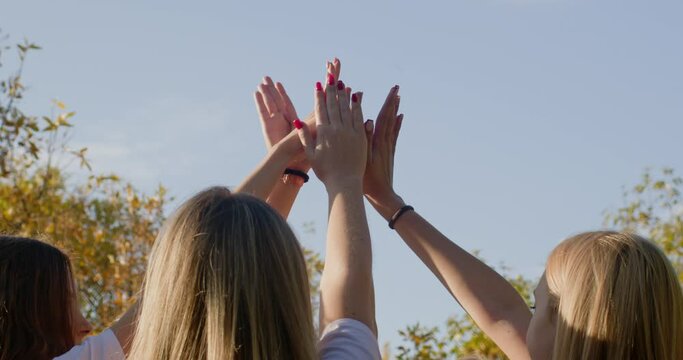 Teenager girls raise hands to sky demonstrating strong connection and unity in park. Group of teens symbolizes connecting friendship backside view