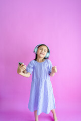 Pretty little girl holding a phone, wearing headphones, and dancing to her music. 