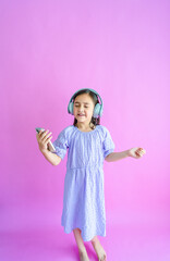 Pretty little girl holding a phone, wearing headphones, and dancing to her music. 
