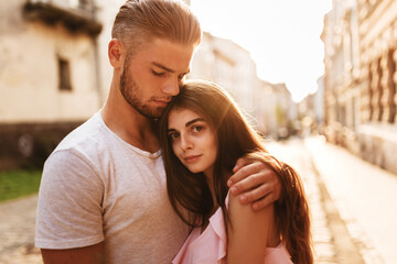 young blond man in a T-shirt hugs a girl in a dress at sunset