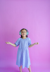 Pretty little girl wearing a purple dress and headphones while dancing to music. 