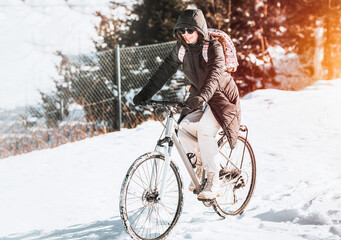 Caucasian girl cycling on snow road with a bicycle. Winter bike sport fun happy cyclist. Happy woman riding a bike in the forest.